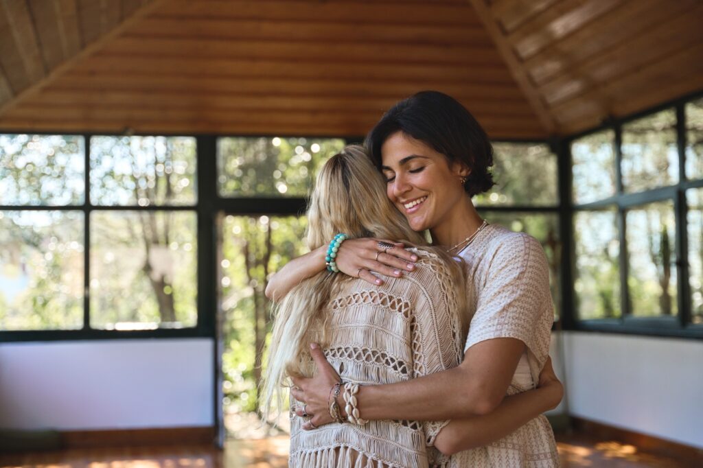 Happy female holistic coach hugging young woman during therapy practice.